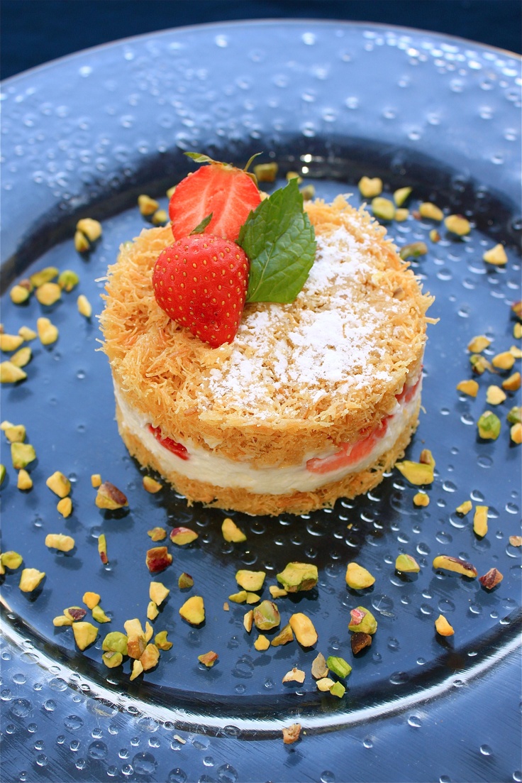 a small dessert on a blue plate with nuts and strawberries around the edges, topped with a strawberry