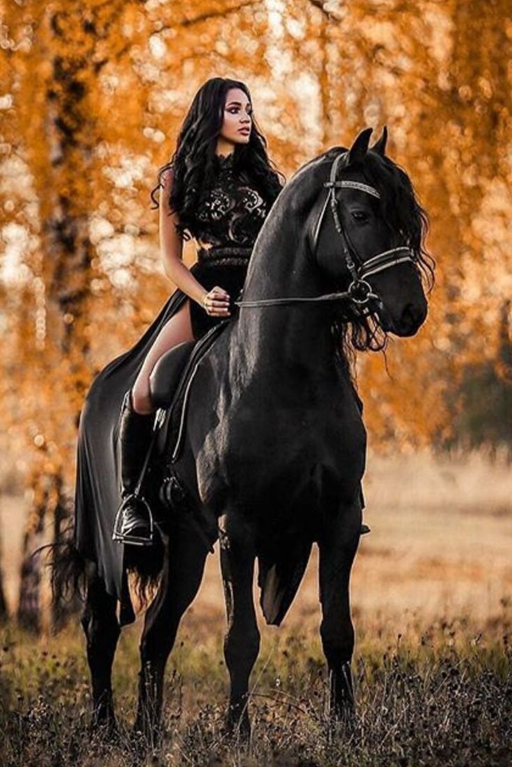 a woman riding on the back of a black horse in an open field with trees