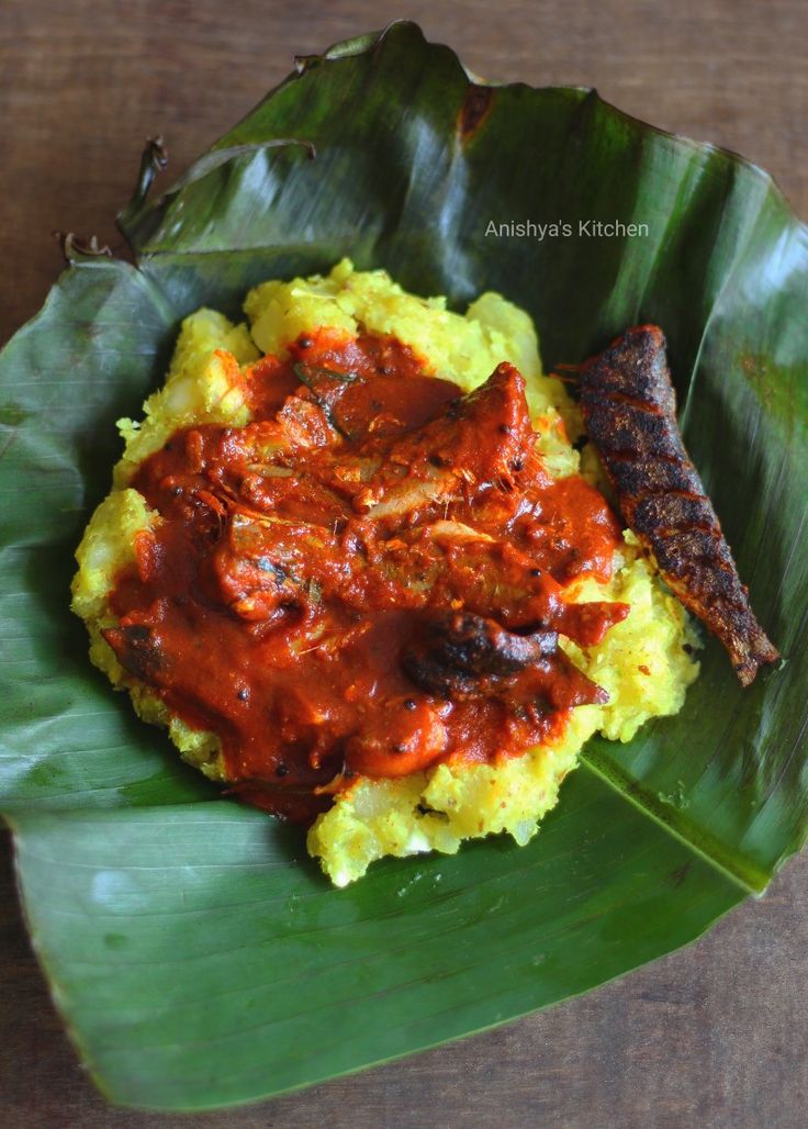 a plate with meat and sauce on top of mashed potatoes next to a green leaf