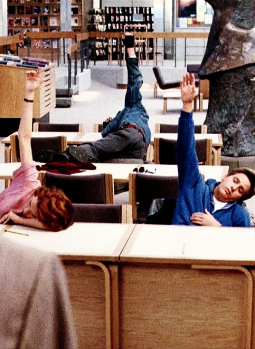 two people laying on desks with their hands in the air