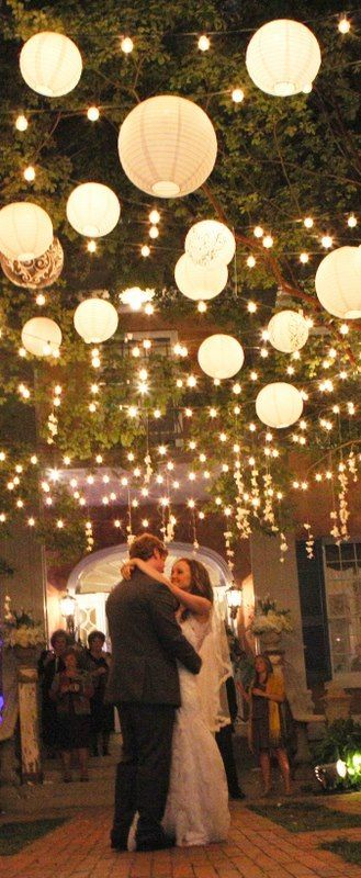 a bride and groom sharing their first dance under lanterns