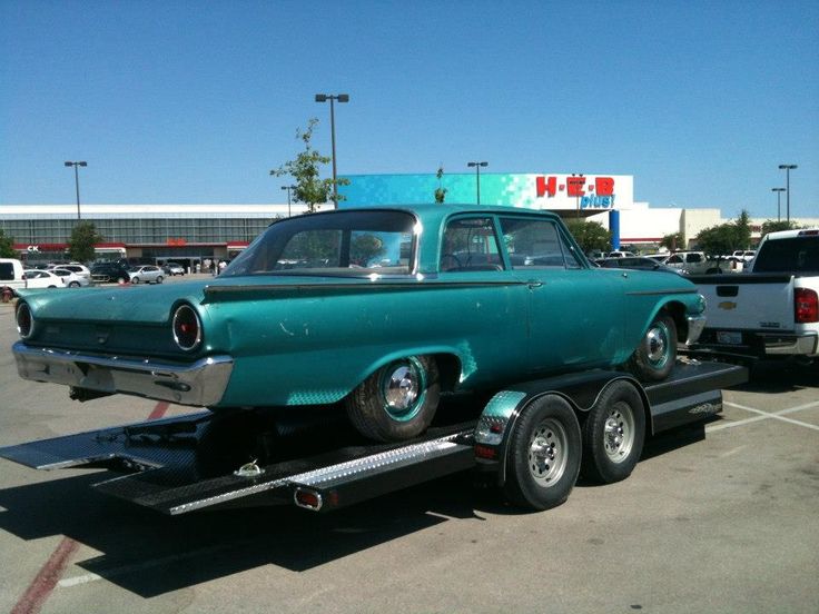 an old green car is on the back of a flatbed truck in a parking lot