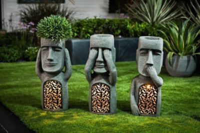 three stone statues with plants growing out of their heads on the grass in front of some bushes