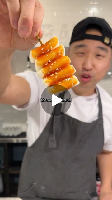 a man holding up food in front of his face while wearing an apron and hat