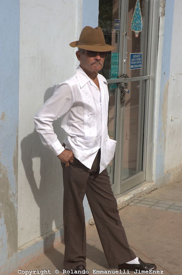 an older man wearing a hat leaning against a wall with his hands on his hips