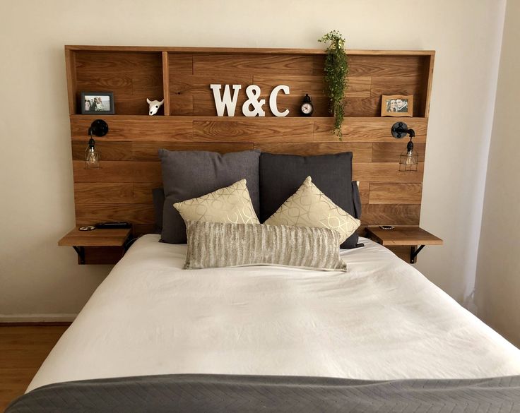 a bed with wooden headboard and pillows on top of it next to a wall mounted shelf