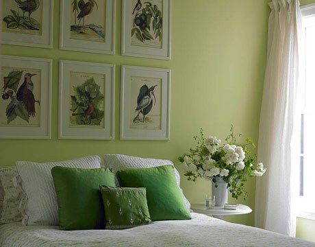 a bedroom with green walls and pictures on the wall above the bed, along with white flowers