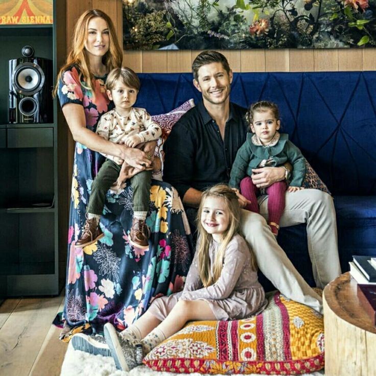 a family sitting on a blue couch in front of a wall with pictures and paintings