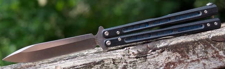 two knives sitting on top of a piece of wood with trees in the back ground