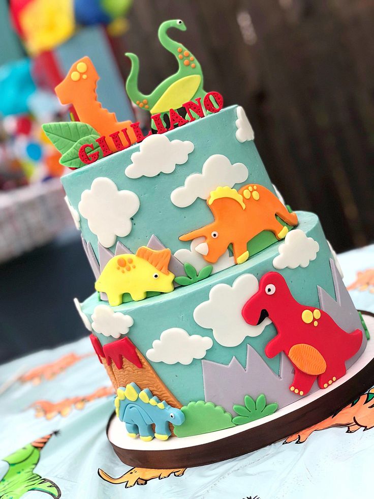 a multi layer cake decorated with dinosaurs and clouds