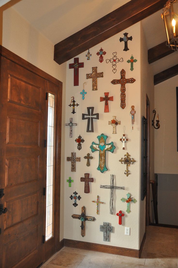 a wall with many crosses on it next to a wooden door and light fixture in the corner