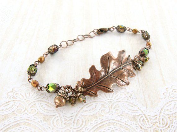 To make this vintage inspired woodland bracelet, I paired delicate copper filigree with woodland hued Czech fire polished beads. The focal is a beautifully detailed antique copper oak leaf. At the ends of the leaf, I clustered dainty little beads with copper acorn-style caps. At one side of the leaf, I included a lovely little acorn charm. The more sparkly beads have a lovely coating on them featuring shades of olivine, copper and red -- the coating is metallic on one side of the bead, and when Antique Copper Jewelry, Woodland Autumn, Autumn Jewelry, Rustic Autumn, Copper Leaf, Cluster Bracelets, Leaf Bracelet, Rustic Jewelry, Leaf Jewelry