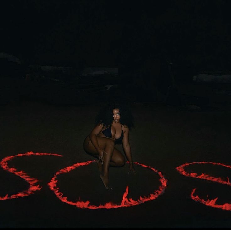 a woman kneeling on the ground in front of some red fire circles with her legs spread out