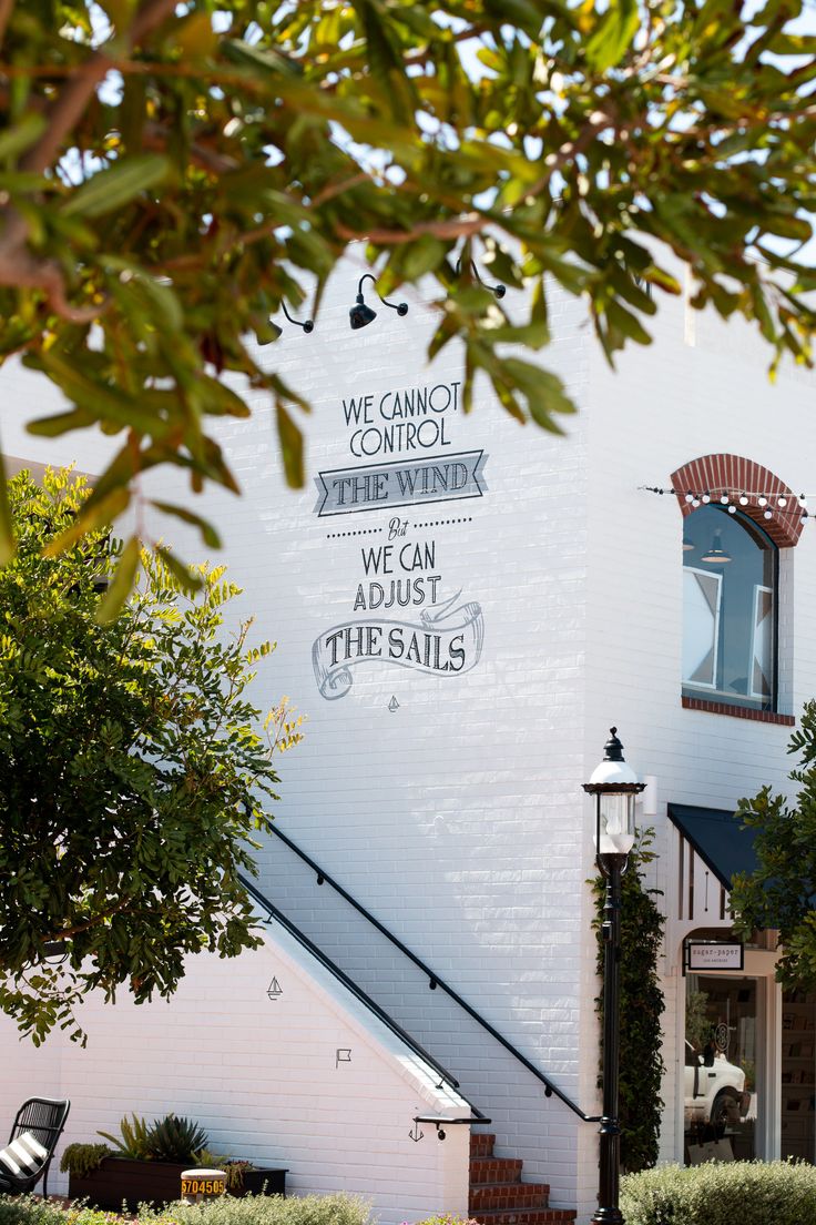 a white building with a sign on the side and trees around it that says we cannot control the wind, we can adjust the sails