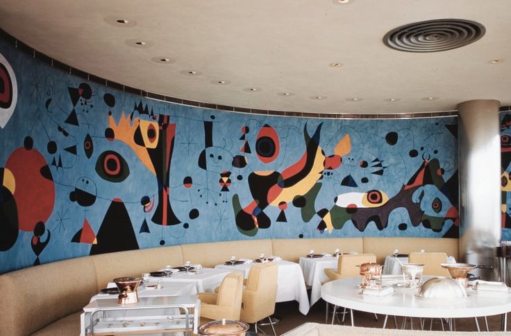 an empty restaurant with tables and chairs in front of a colorful mural on the wall