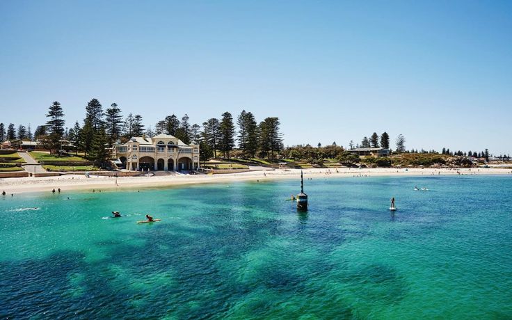 people are swimming in the ocean near a beach with houses and pine trees on it