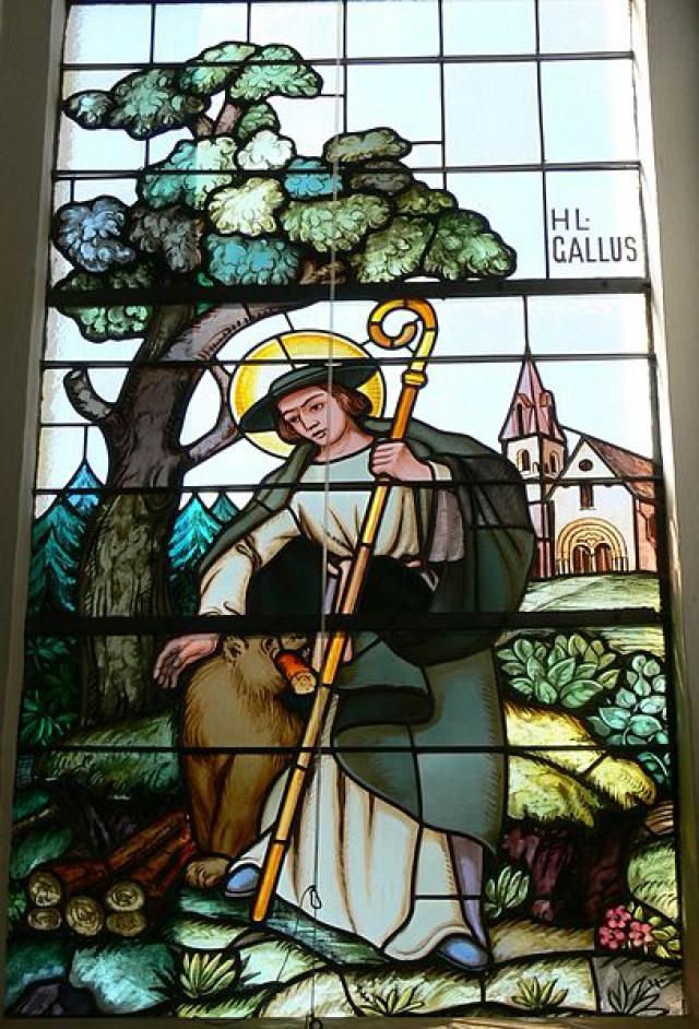 a stained glass window with a person holding a cross and a tree in the background