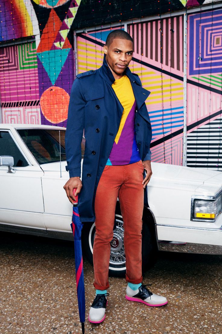 a man standing in front of a white car wearing colorful socks and an overcoat