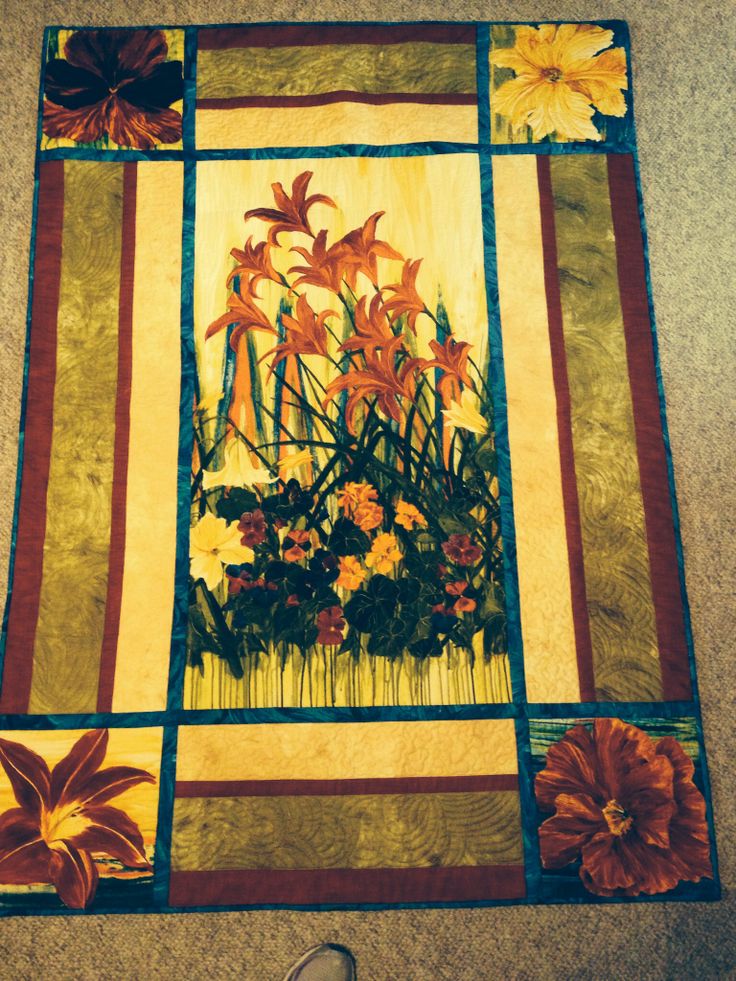 a quilted wall hanging with flowers and leaves on it's side, along with a pair of shoes