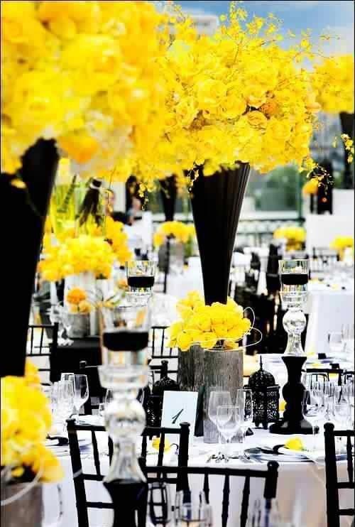 yellow flowers are in tall black vases on the tables at a wedding reception with white tablecloths