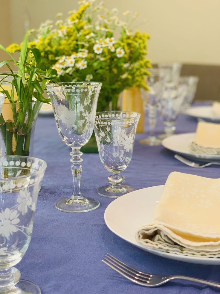 the table is set with glasses, plates and flowers in vases on top of them