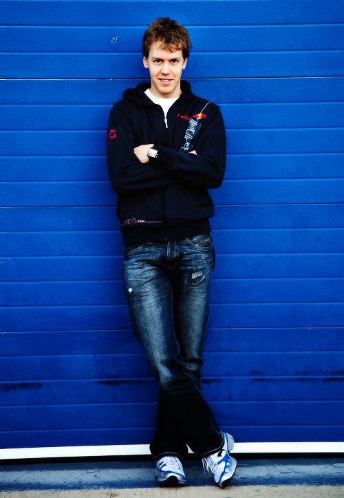 a man standing in front of a blue wall with his arms crossed and looking at the camera