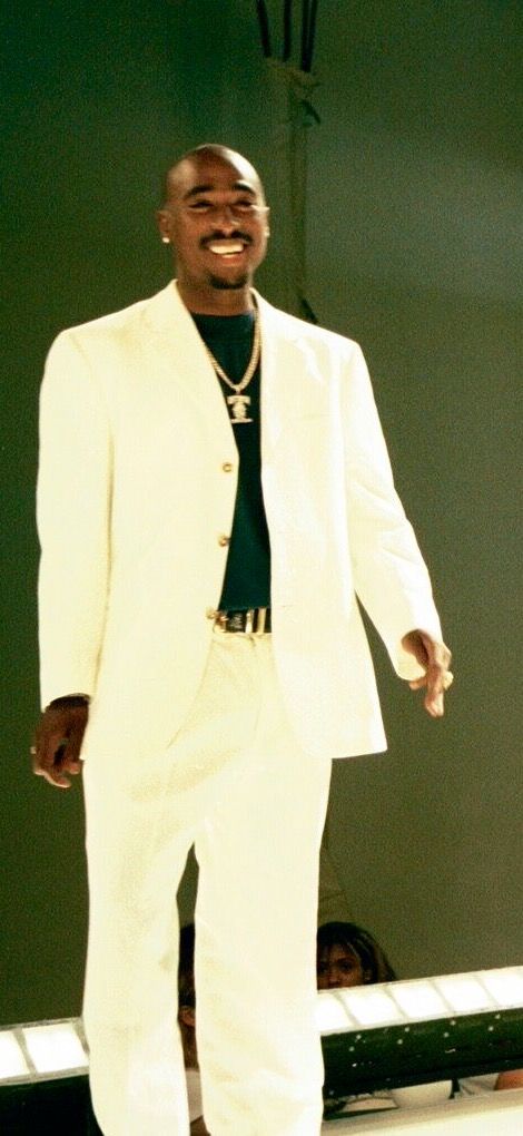 a man in a white suit and tie walking down the runway at a fashion show