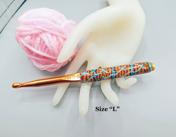 a pink ball of yarn next to a crochet hook with a gold handle