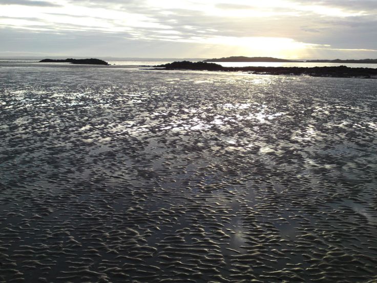 the sun shines brightly through the clouds over an ocean beach with small islands in the distance