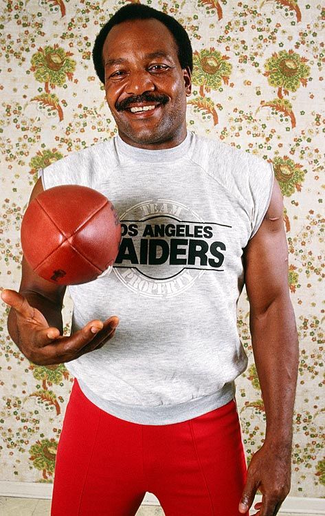 a man holding a basketball in his right hand and smiling at the camera with both hands