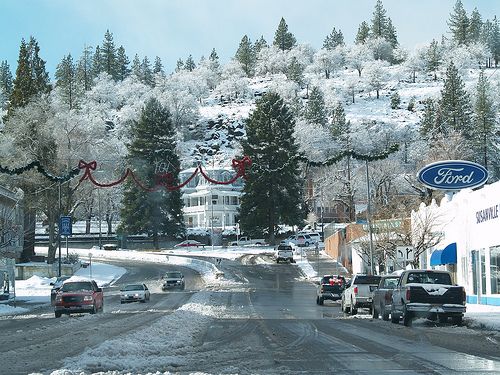 cars driving down a snowy road with christmas decorations on the trees