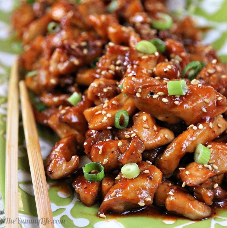 chicken with sesame seeds and green onions served on a green platter next to chopsticks