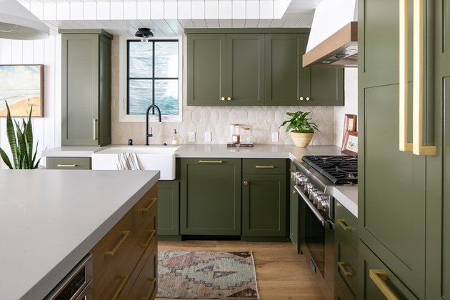 a kitchen with green cabinetry and white counter tops, along with an area rug on the floor