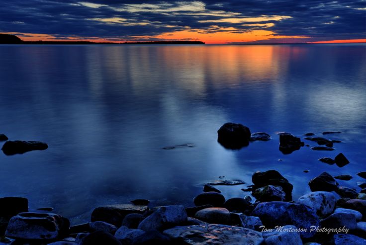 the sun is setting over the ocean with rocks in the foreground and clouds in the background