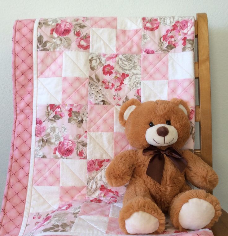 a brown teddy bear sitting next to a pink and white quilted wall hanging on the wall