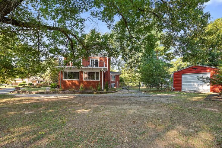 a red house sitting in the middle of a field next to a tree and two garages