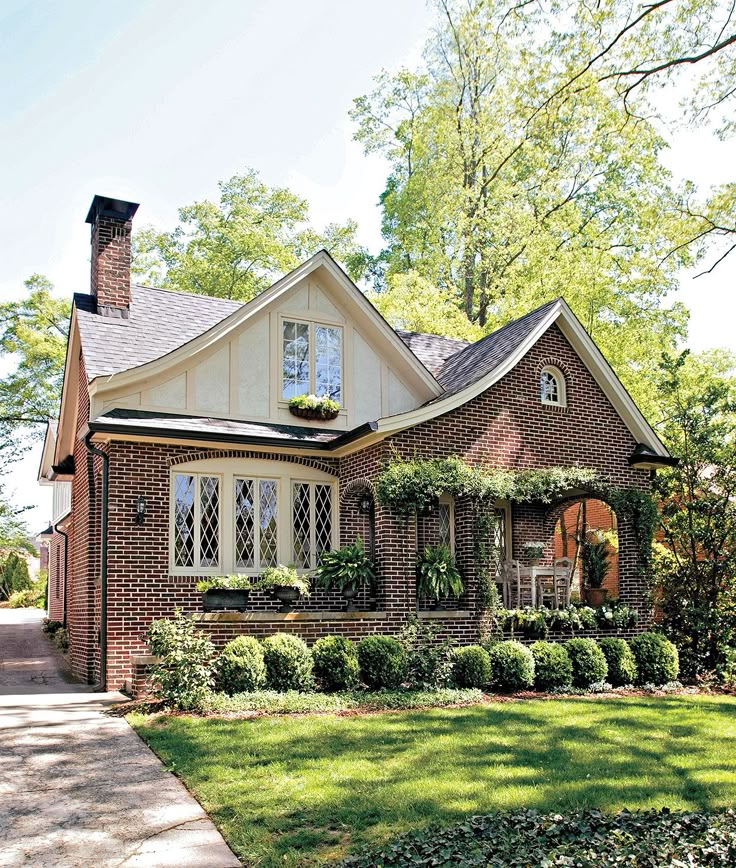 a brick house with white trim and lots of greenery on the front lawn,