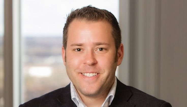 a man wearing a suit and tie in front of a window smiling at the camera