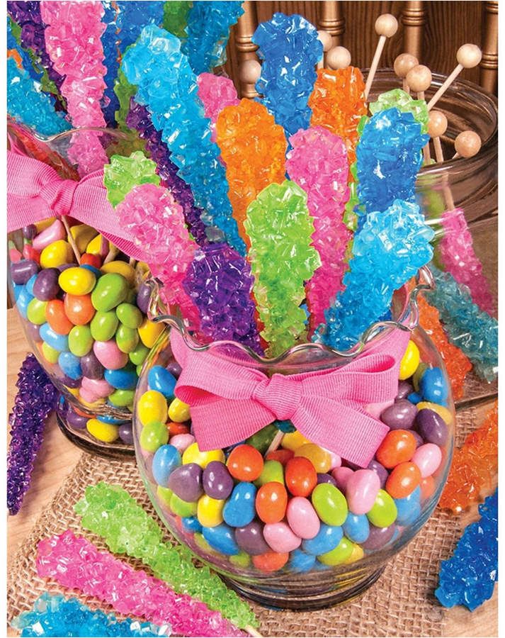 colorful candies are in a glass bowl on a table next to candy sticks and lollipops