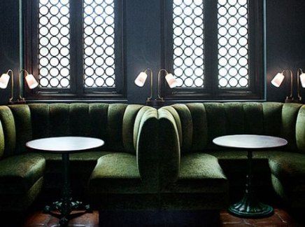 two tables are sitting in the corner of a booth with green velvet upholstered couches