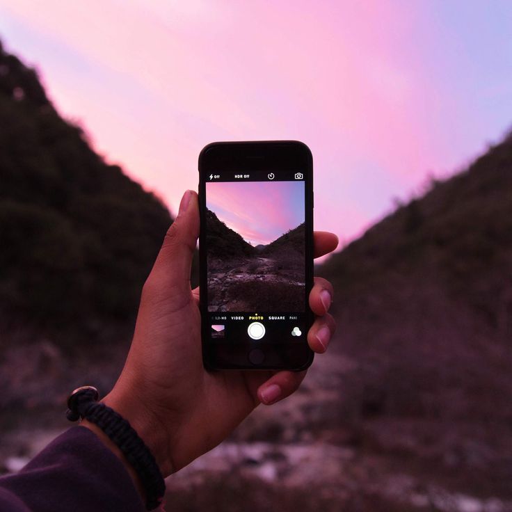 someone holding up their cell phone to take a photo with the mountains in the background