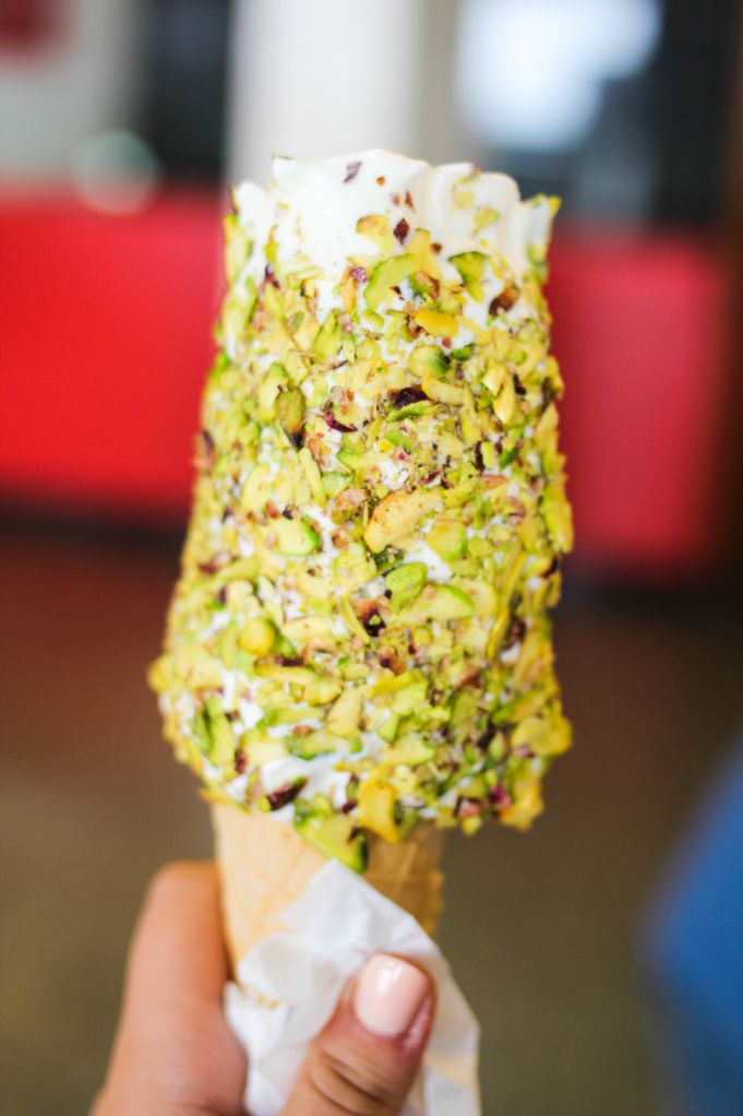 a person holding an ice cream cone with pistachio and nuts on it's tip