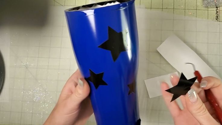 two hands are holding black stars on a blue tumbler with white tiles in the background