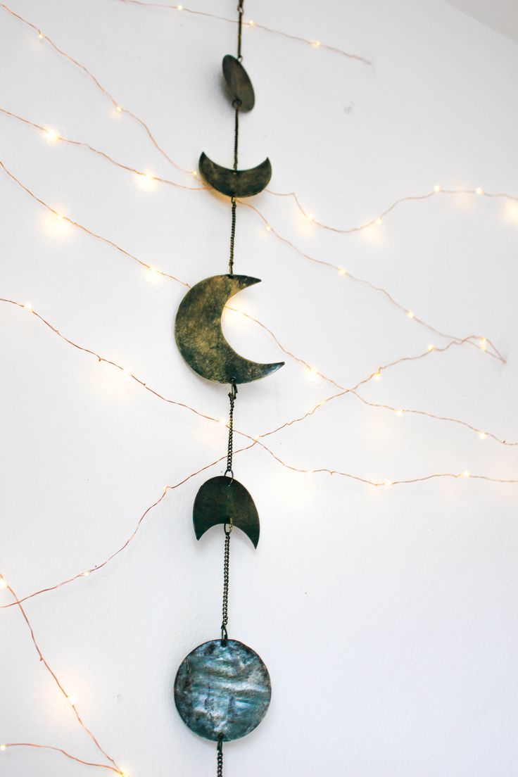 a metal wind chime with three crescents hanging from it's sides and lights on the wall behind it