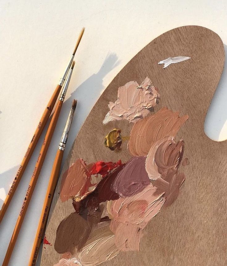 an artist's palette and two paintbrushes on a white surface with brown paper