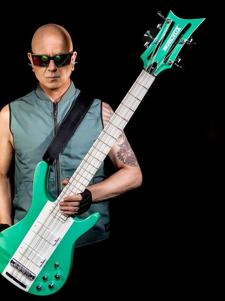 a man holding a green guitar in his right hand and wearing sunglasses on the other