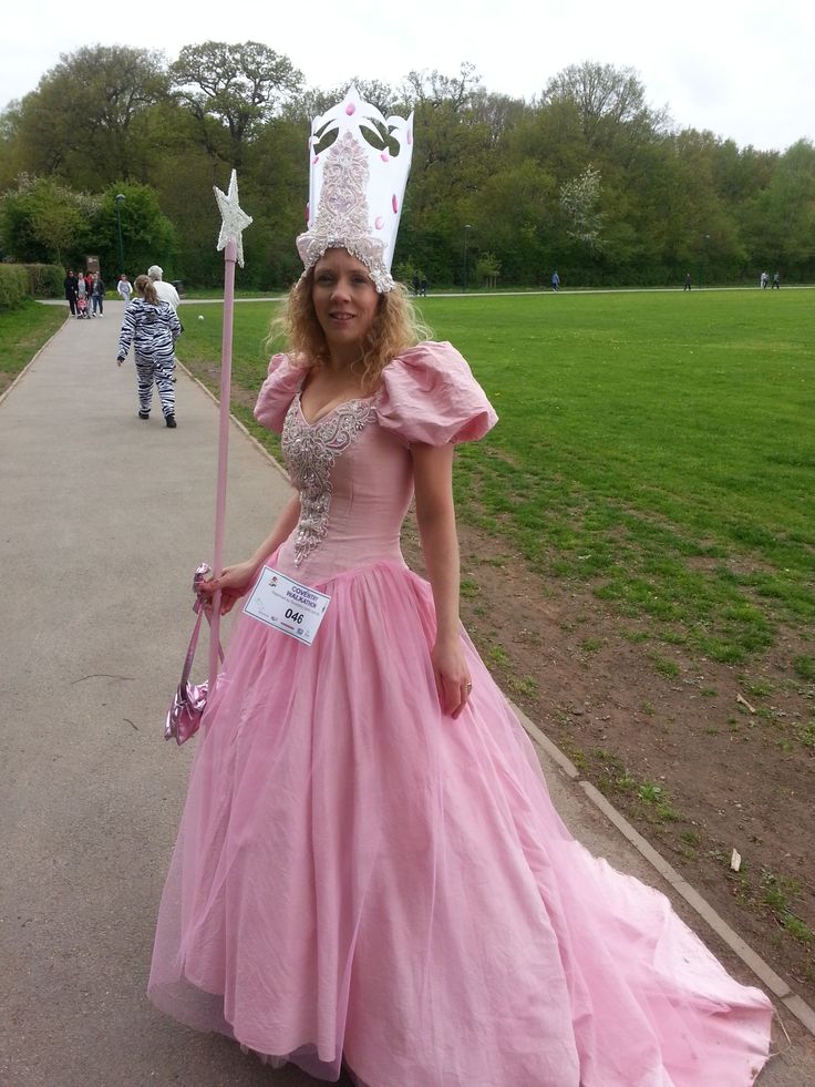 a woman in a pink ball gown and tiara holding a wand on the sidewalk