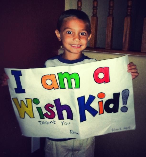 a young boy holding up a sign that says i am a wish kid