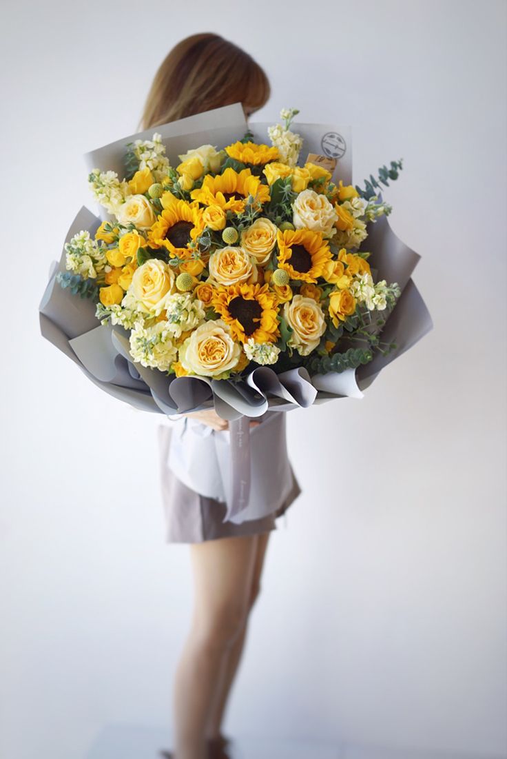 a woman holding a bouquet of sunflowers and roses