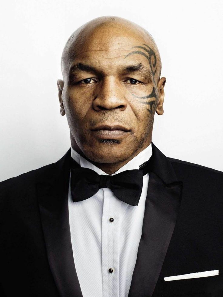 a bald man in a tuxedo with tattoos on his face and chest is looking at the camera